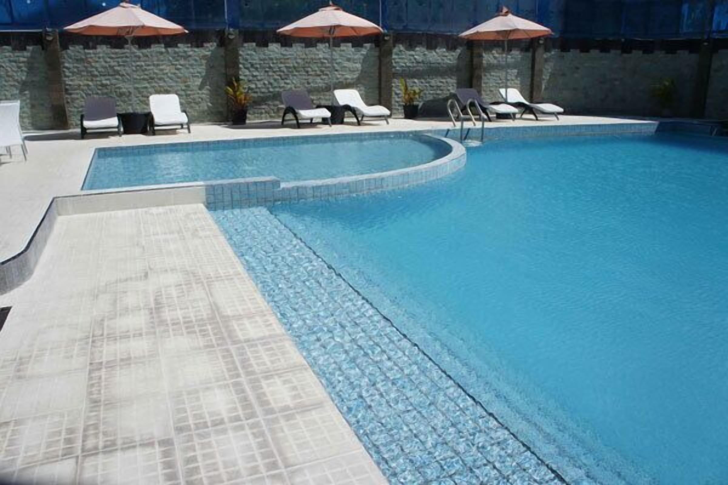 A swimming pool with a tiled deck, lounge chairs, and umbrellas.