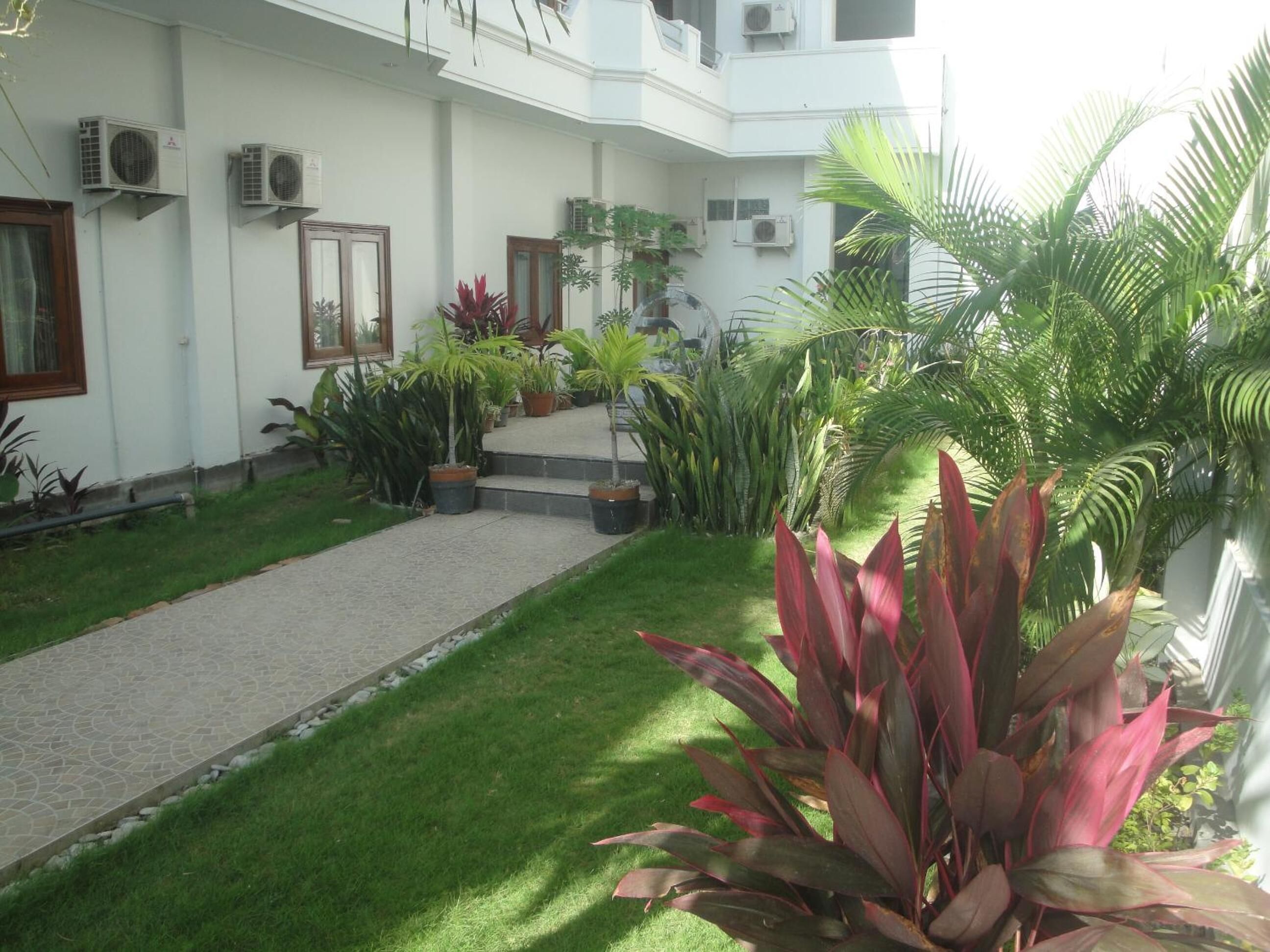 A courtyard with a paved walkway, potted plants, and air conditioning units on the building facade.