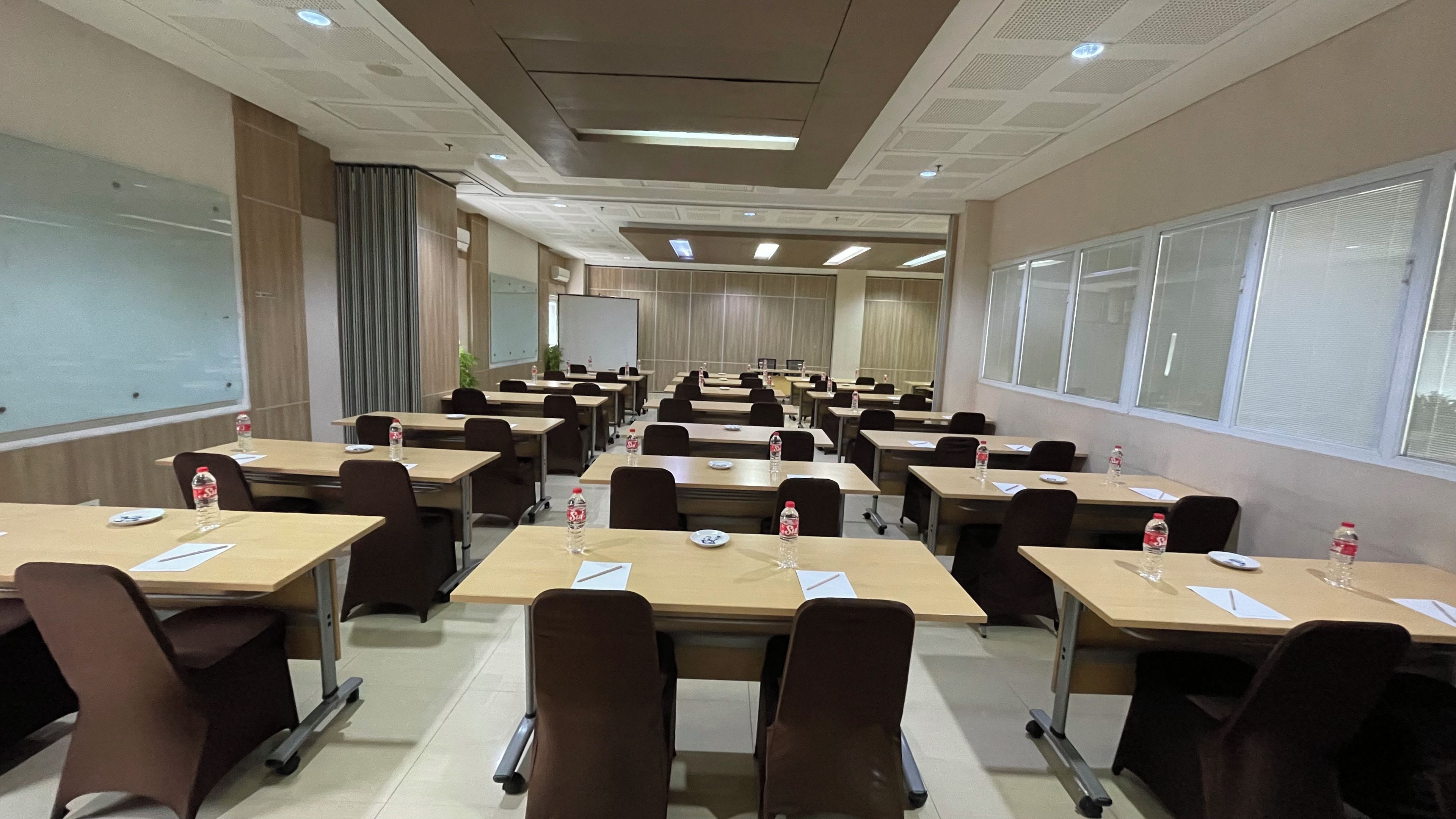Un salón de conferencias con filas de mesas, sillas y botellas de agua.