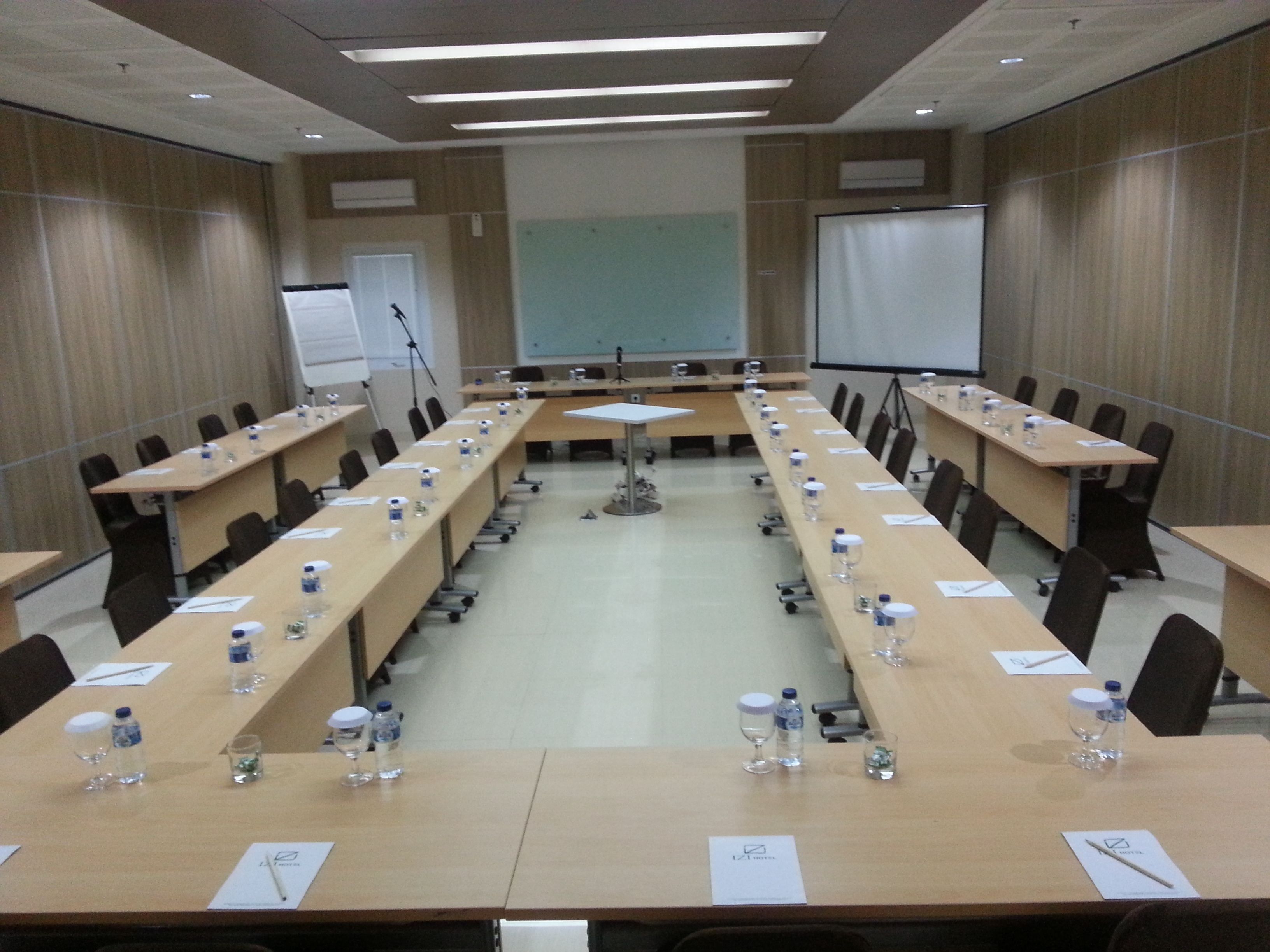 A conference room with long tables, chairs, water bottles, and a projector screen.