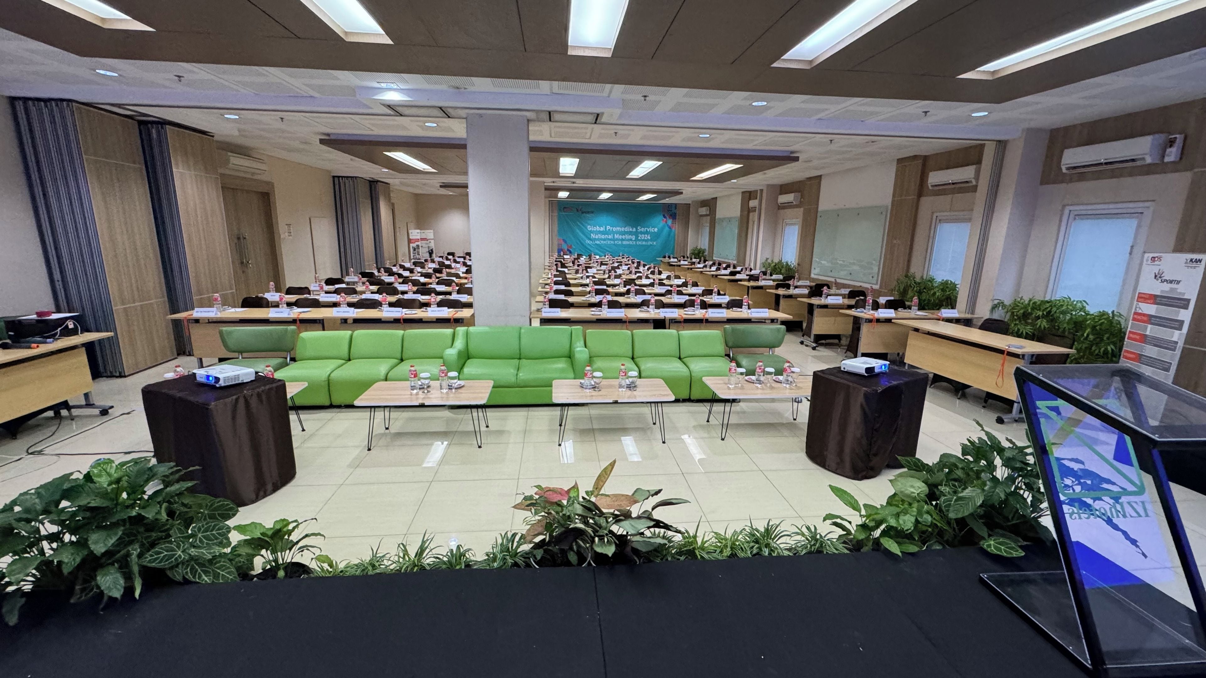 A conference room with rows of tables, a green sofa, and a presentation screen.