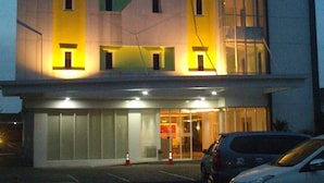 A multi-story hotel with a modern design, featuring a prominent yellow-lit entrance and a visible parking area with several cars. - IZI Hotels (Bogor)