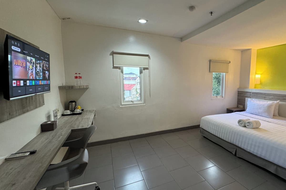A hotel room with a bed, a desk, a TV, and a window.