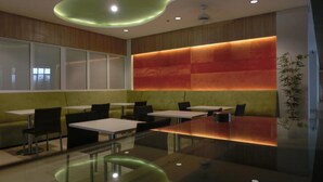 A modern dining area with glass tables and chairs, a wooden accent wall, and a green ceiling feature. - IZI Hotels (Bogor)