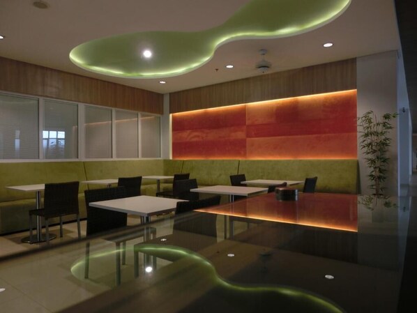 Un'area pranzo moderna con tavoli e sedie in vetro, una parete decorativa in legno e un elemento decorativo al soffitto verde.