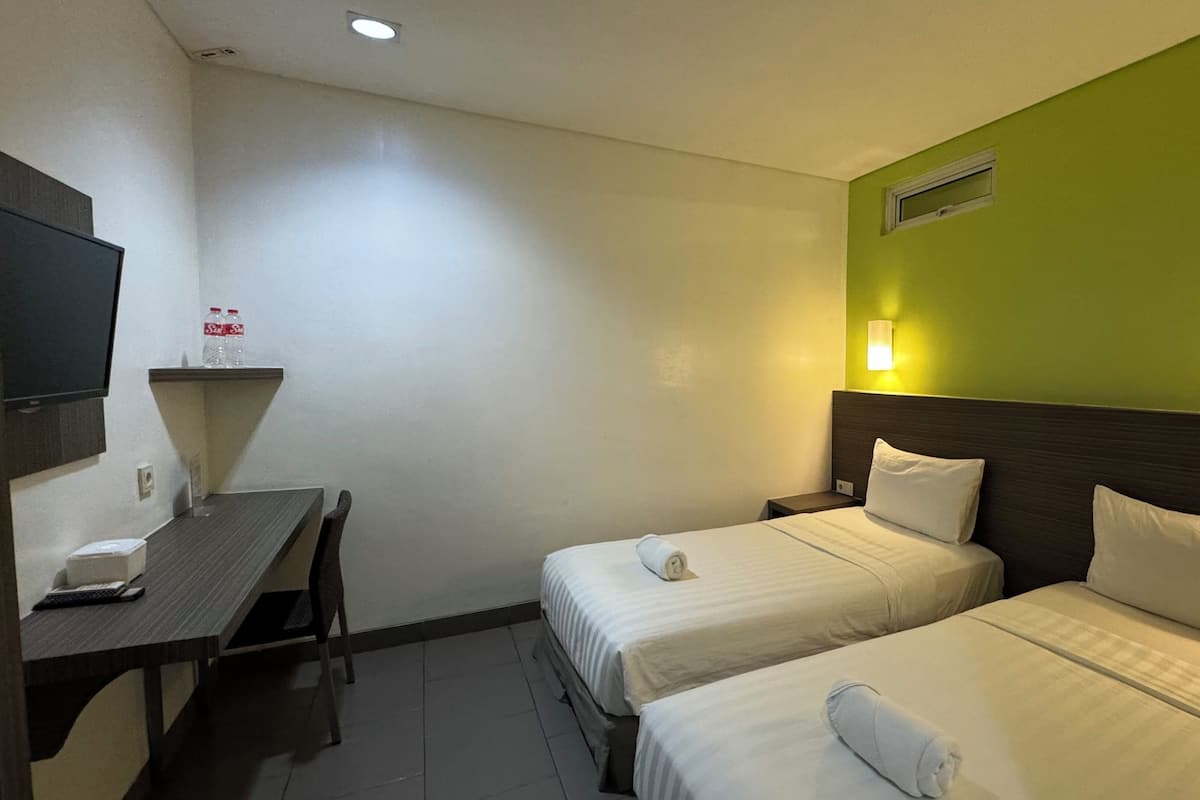 A hotel room with two beds, a desk with a telephone, and a wall-mounted TV.