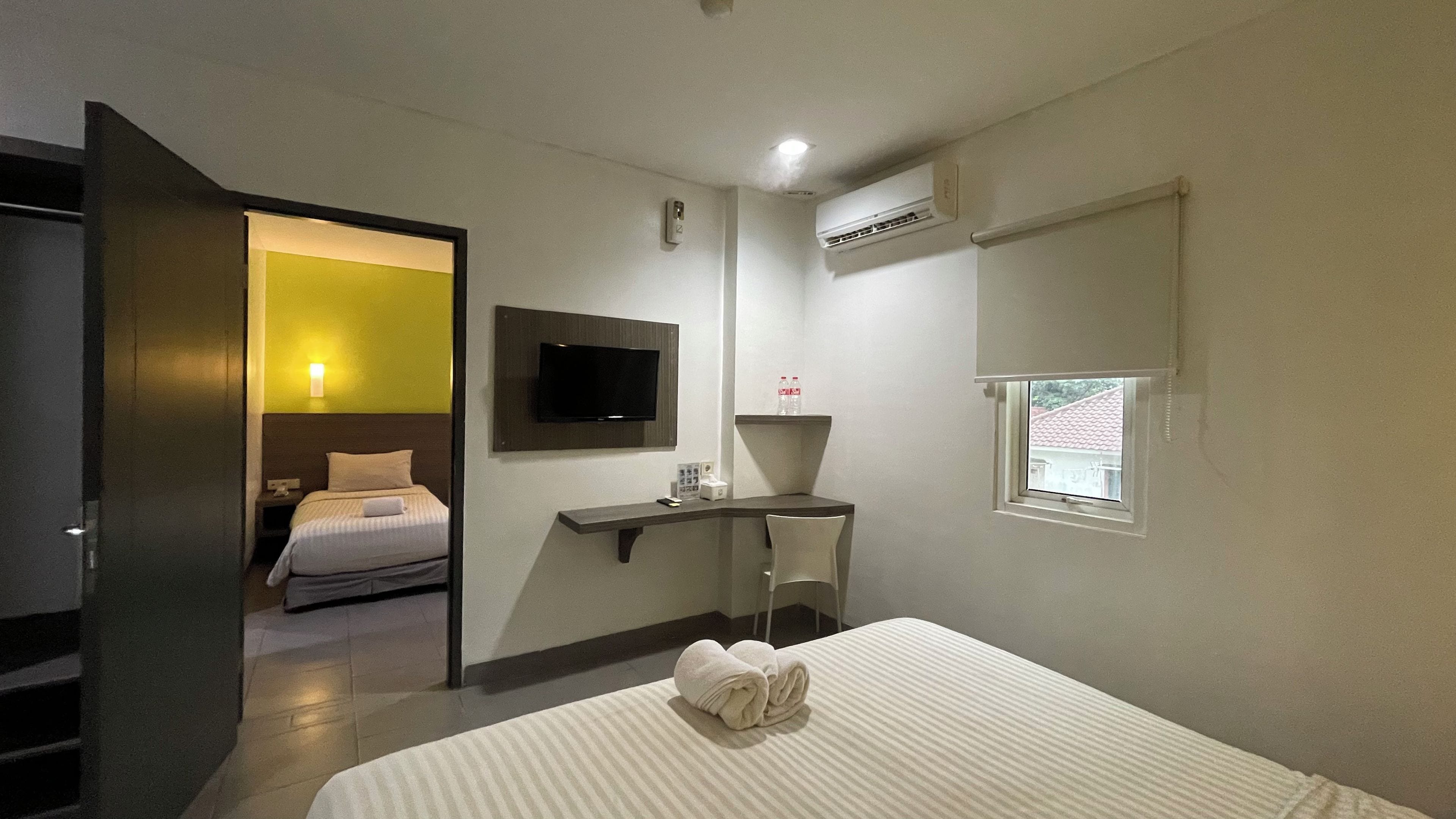 Una habitación de hotel con cama, escritorio, silla, televisor y aire acondicionado.