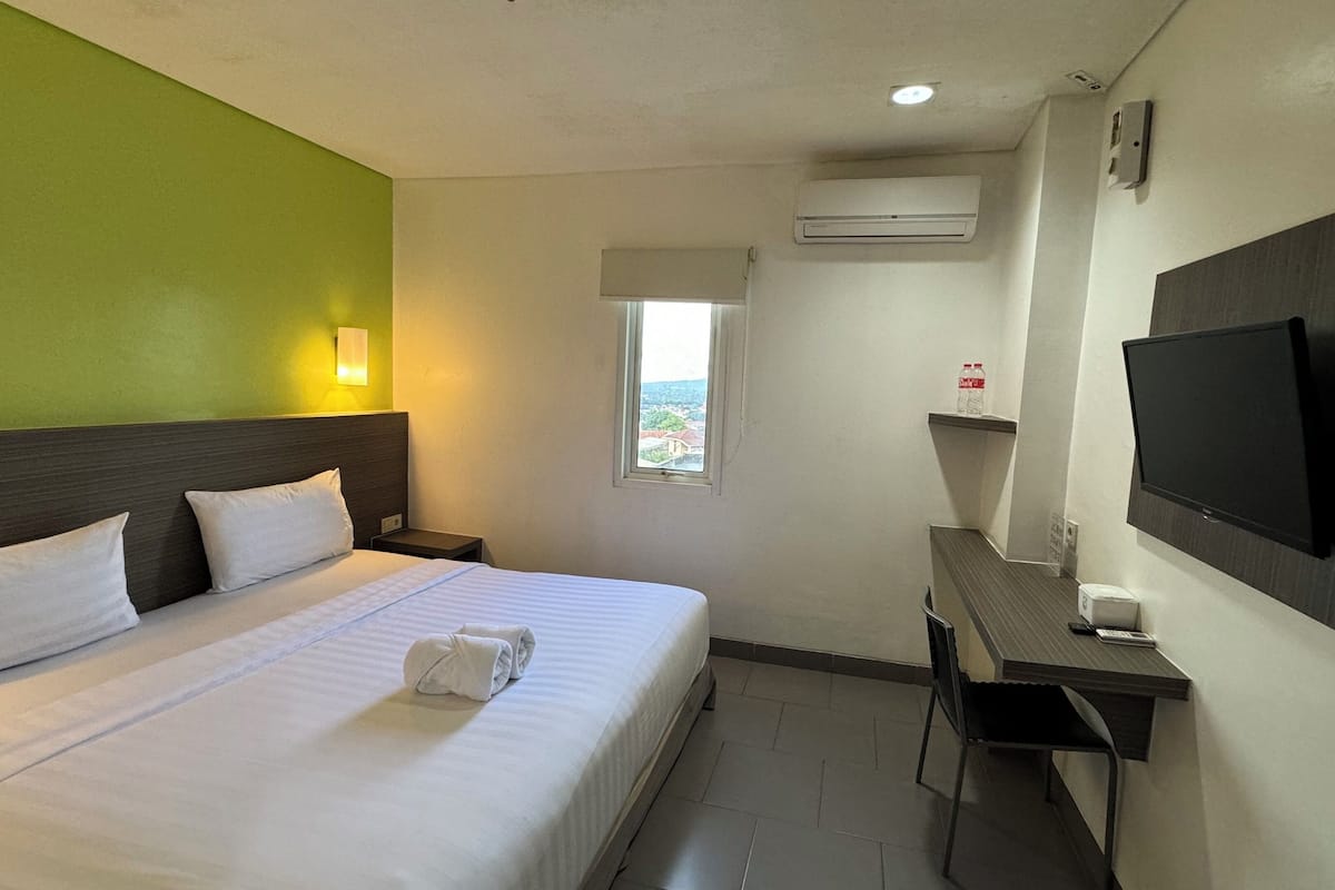 A hotel room with a bed, a desk, a TV, and a window with a view.