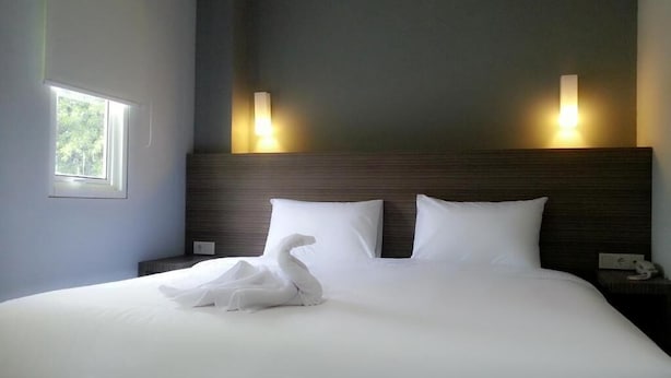 A neatly made bed with white linens and a swan-shaped pillow. There are two wall-mounted lights on either side of the bed. - IZI Hotels (Bogor)