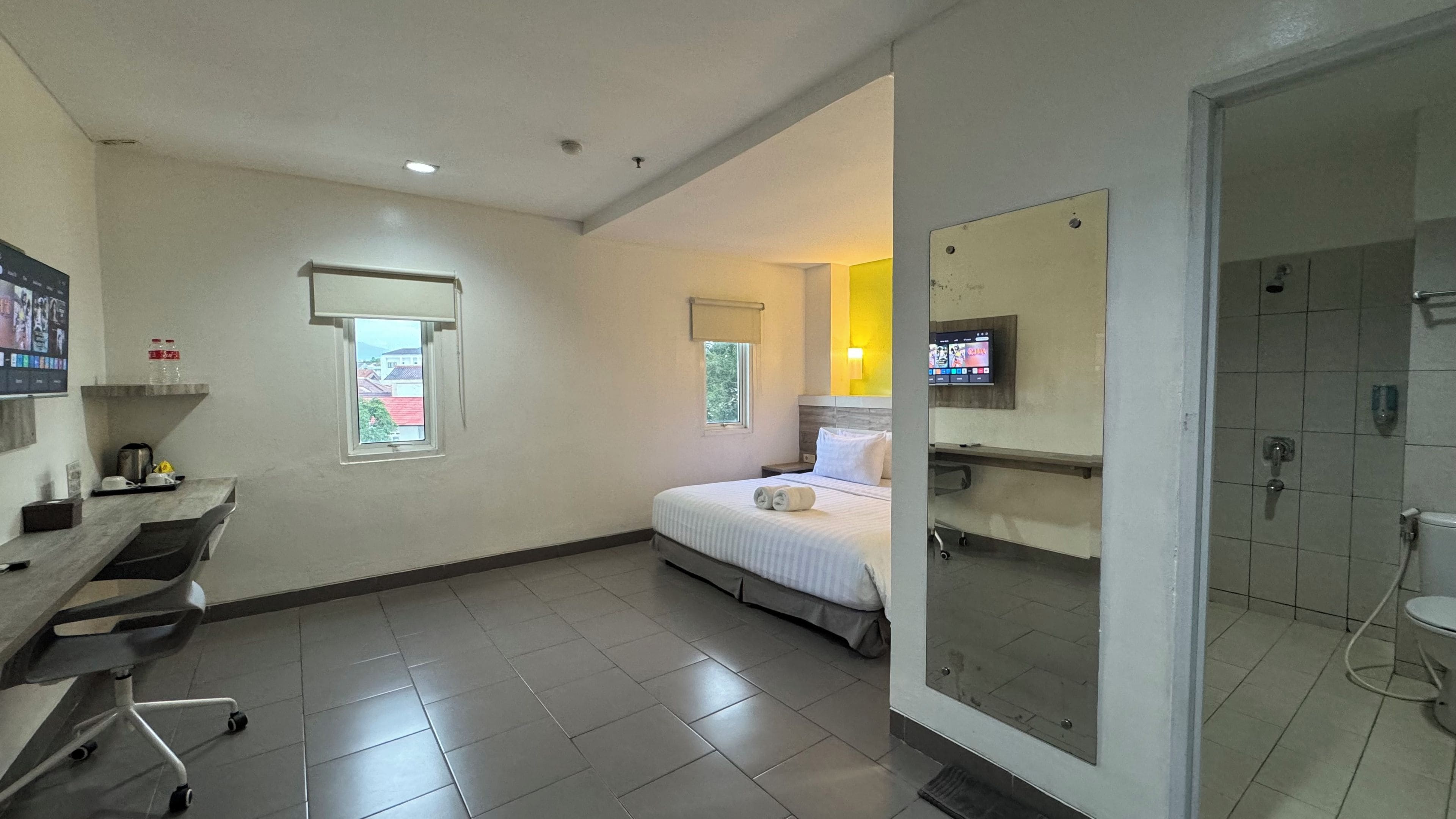 A hotel room with a bed, a desk, a chair, a television, and a shower area.