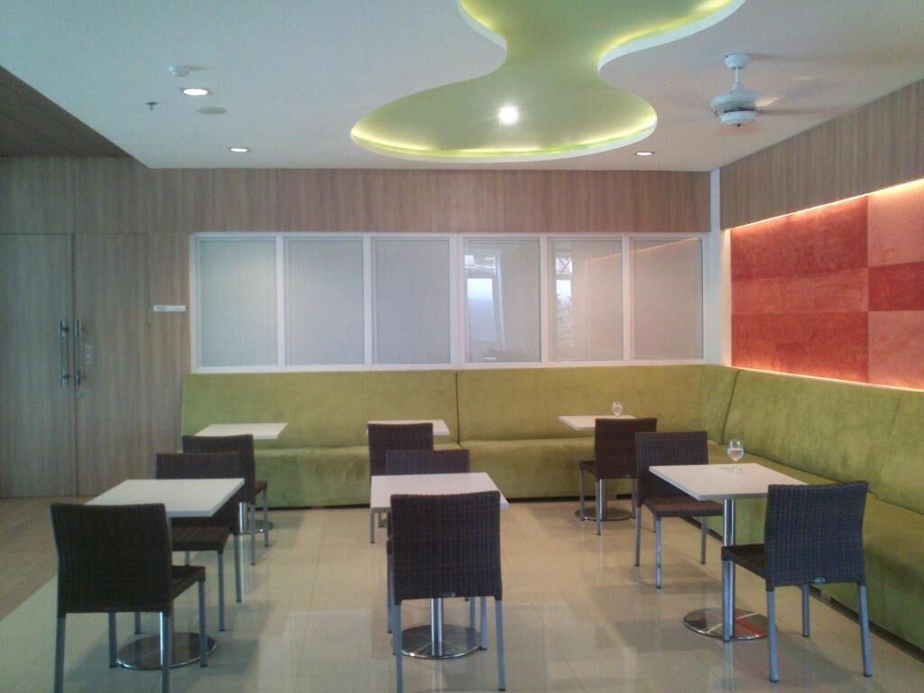 A modern dining area with tables and chairs, a green cushioned bench, and a large window with frosted glass panels.
