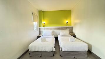Habitación de hotel con dos camas individuales, una mesita de noche con teléfono y una lámpara de pared.