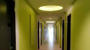 A long, narrow hallway with green walls and a tiled floor, leading to a bright end. - IZI Hotels (Bogor)