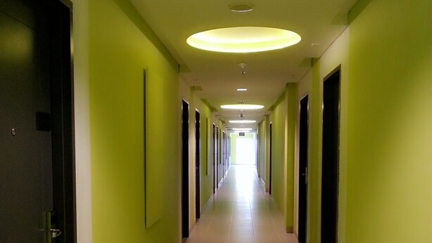 A long, narrow hallway with green walls and a tiled floor, leading to a bright end. - IZI Hotels (Bogor)