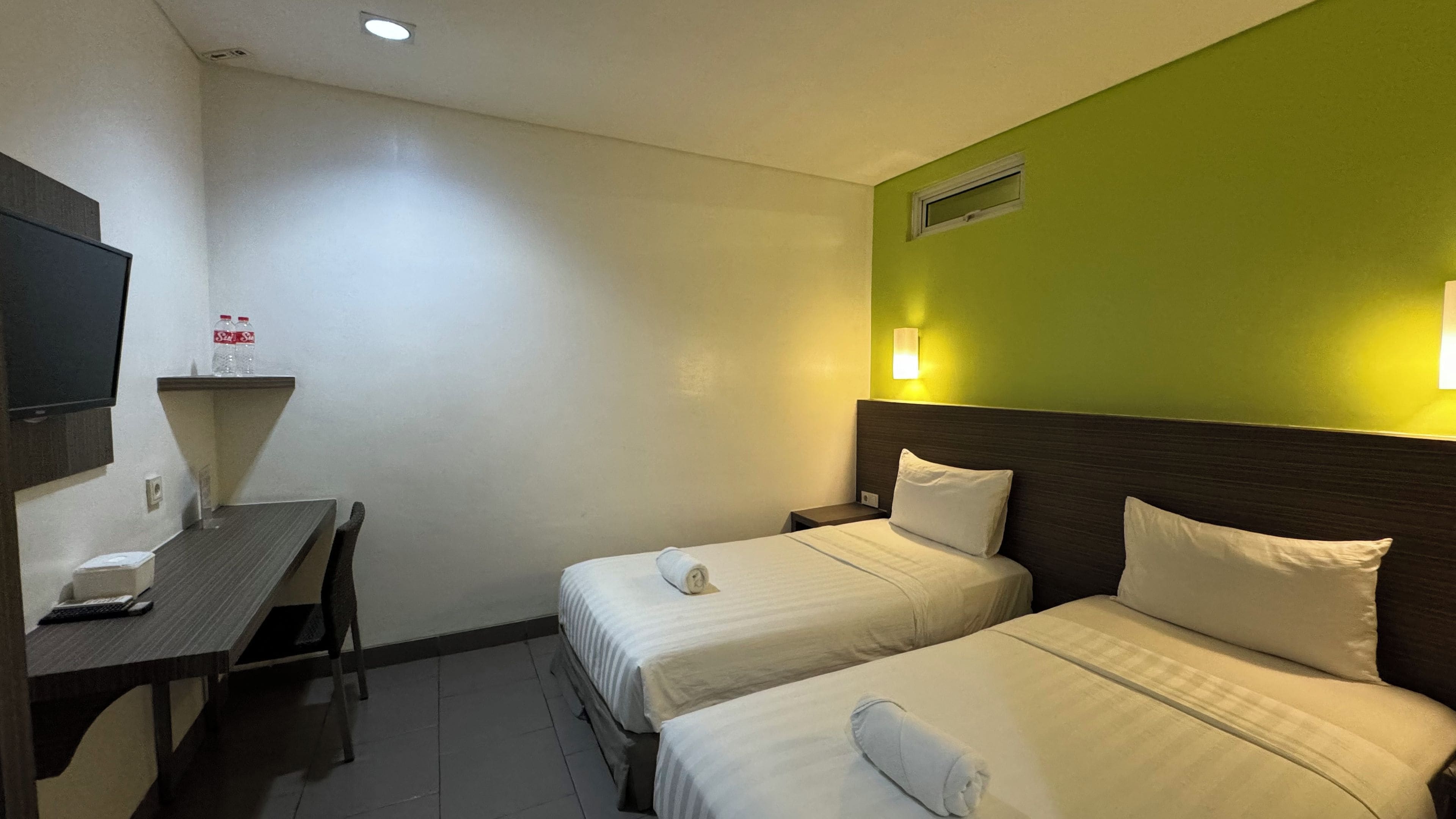 A hotel room with two beds, a desk with a telephone, and a wall-mounted TV.