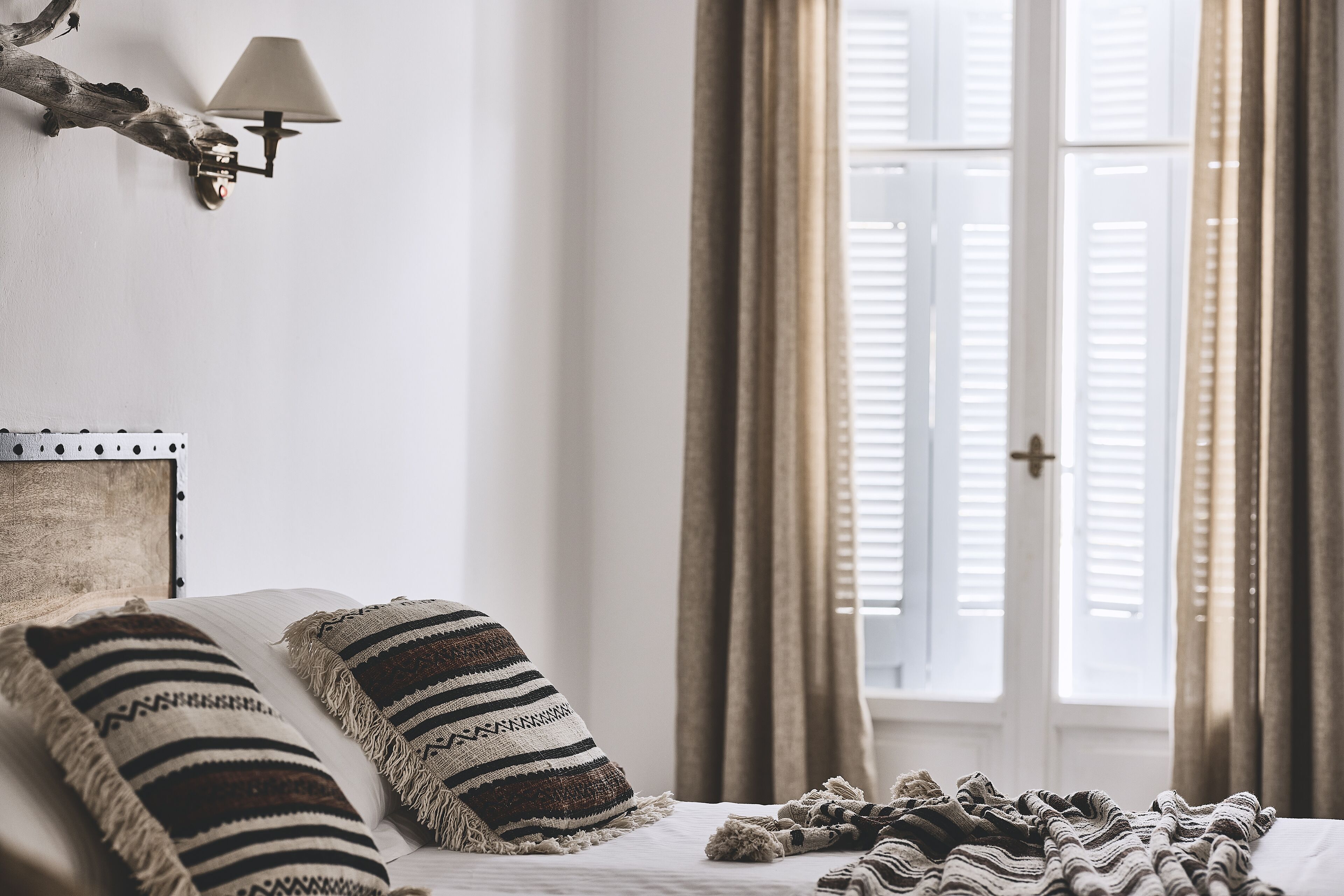 Een slaapkamer met een bed, twee kussens, een lamp en een raam met gordijnen.