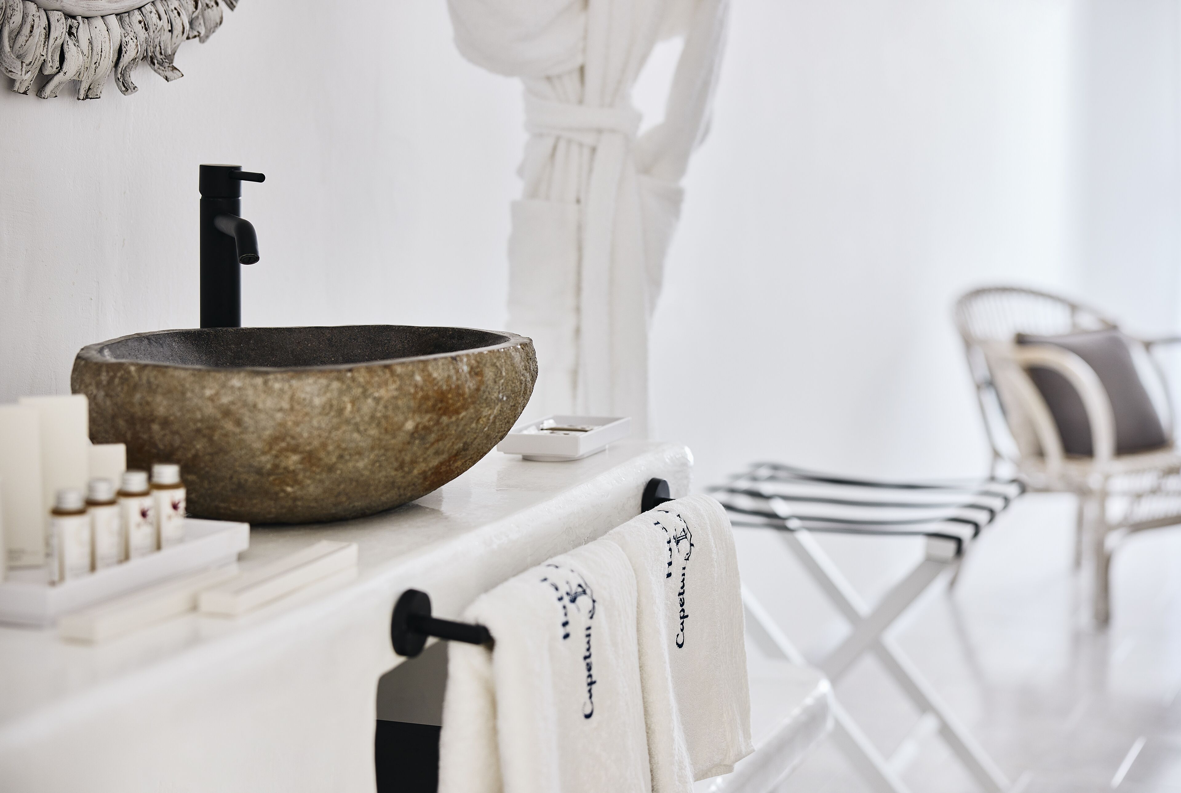 A bathroom with a stone sink, white towel rack, and a chair.