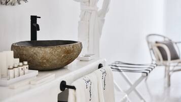 A bathroom with a stone sink, white towel rack, and a chair.