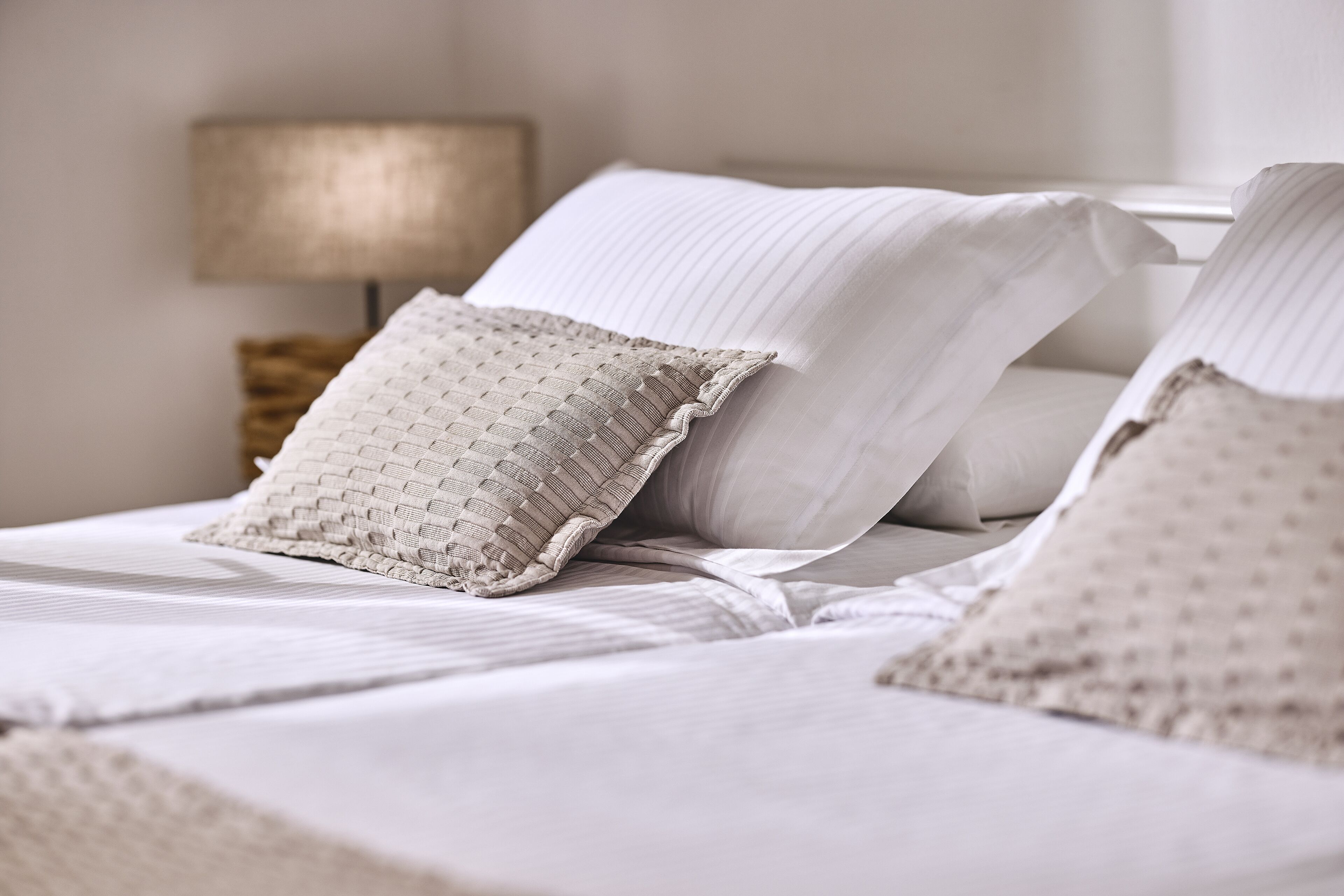 A neatly made bed with white linens and a textured pillow.