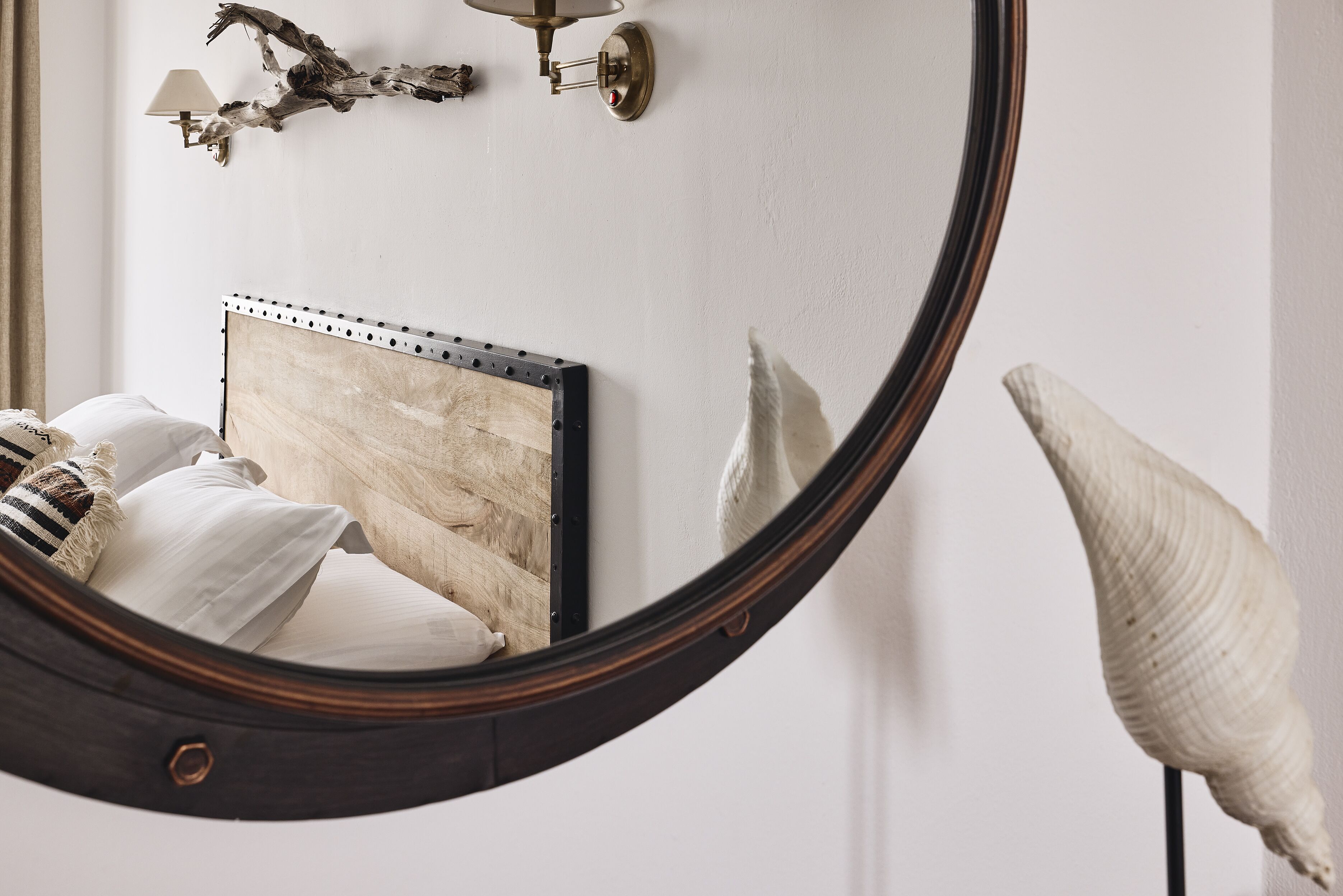 A bedroom with a wooden headboard, a round mirror, and a decorative shell.