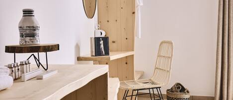 Une coiffeuse en bois avec un miroir, une bouteille et des articles de toilette. Une chaise en osier et un panier tressé sont posés sur le sol.