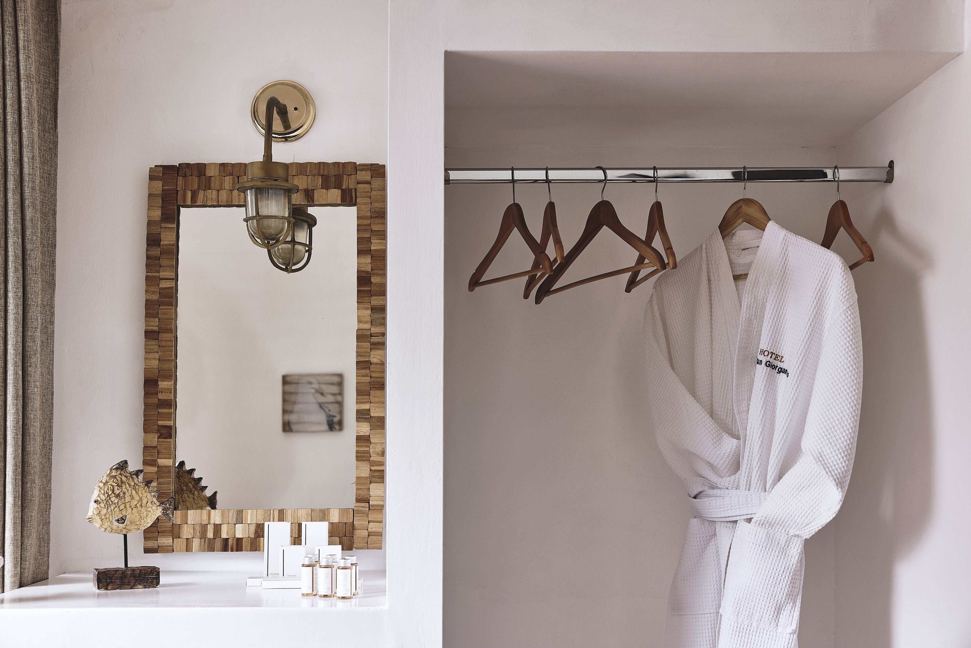 Un baño con pared de mosaicos de madera, un espejo, un perchero de toallas con colgadores de madera y una bata blanca colgada en el perchero.