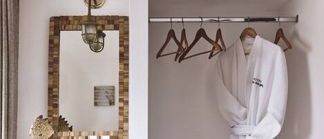 A bathroom with a wooden mosaic wall, a mirror, a towel rack with wooden hangers, and a white robe hanging on the rack.