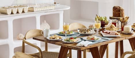 A breakfast setting with a wooden table, wicker chairs, and a variety of food and drinks.