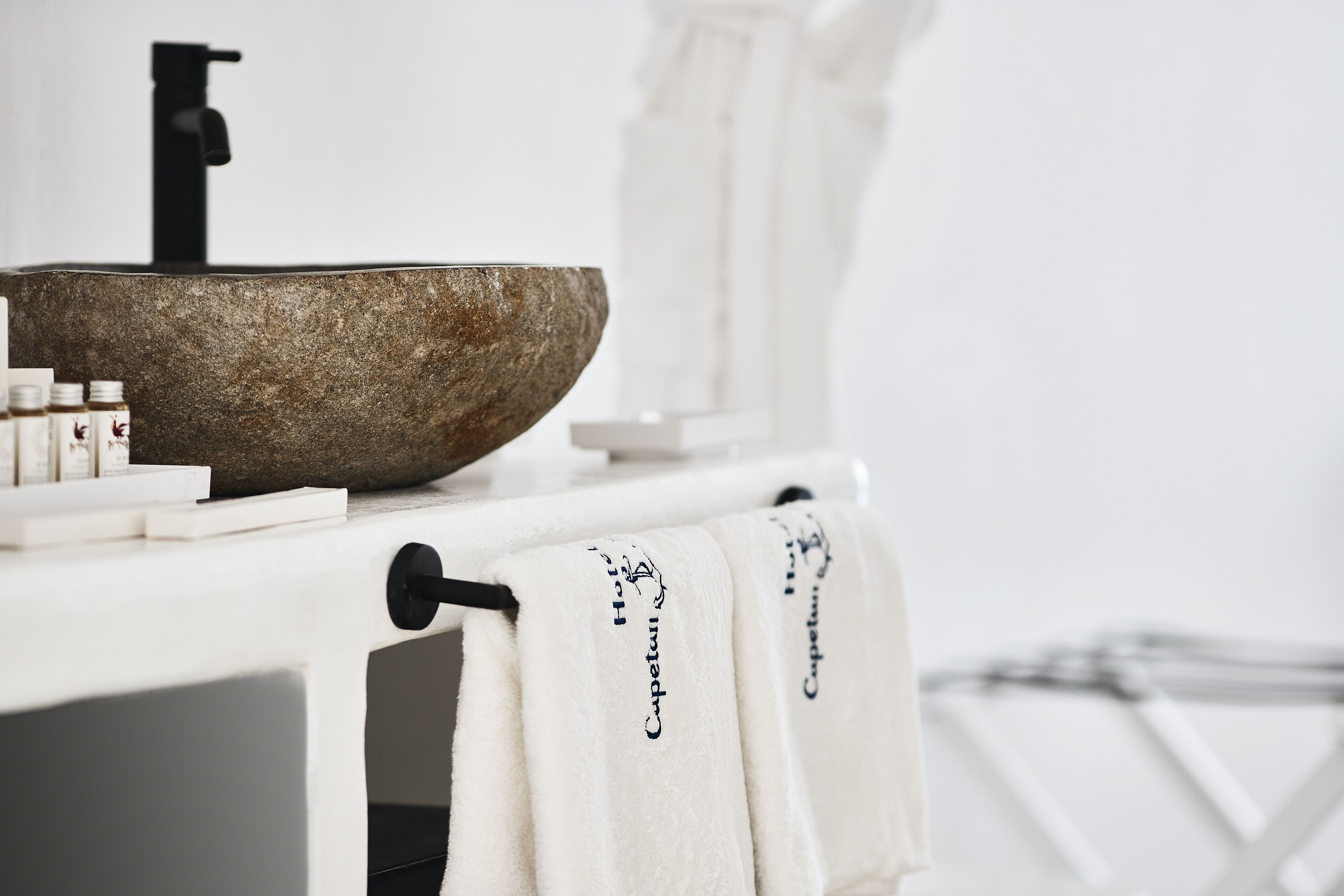 A bathroom with a stone sink, white towel racks, and neatly arranged toiletries.
