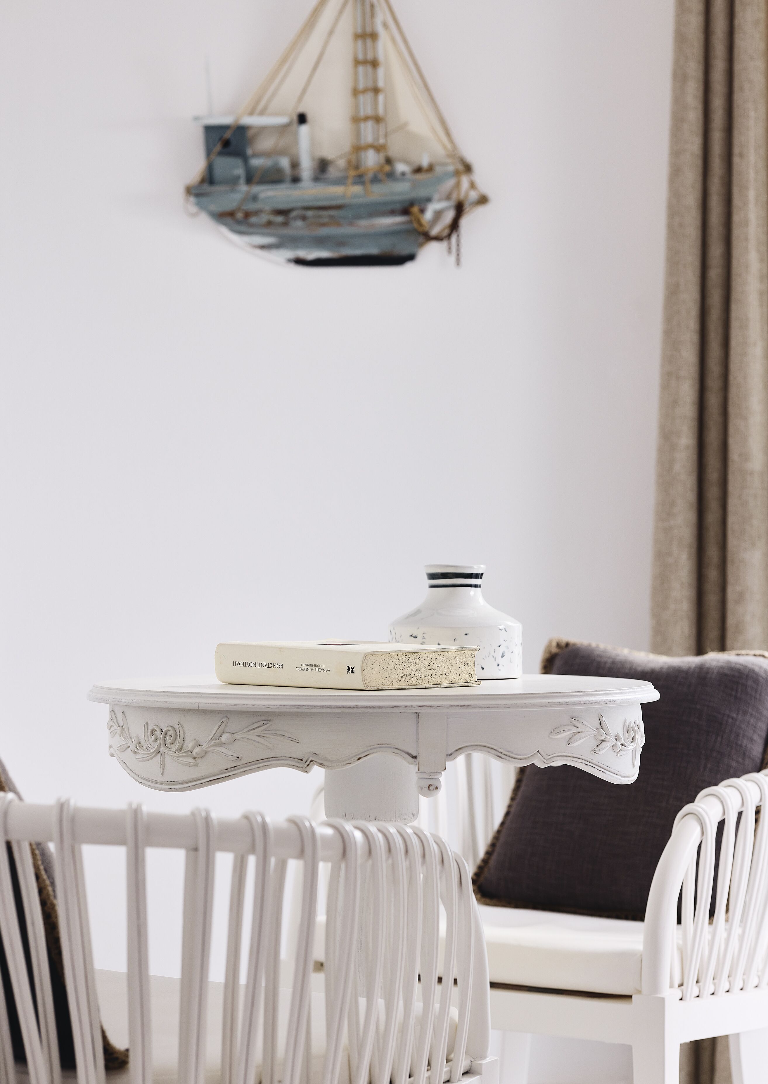Une table blanche avec un plateau décoratif, une chaise blanche avec un dossier incurvé et un petit objet décoratif posé sur la table.