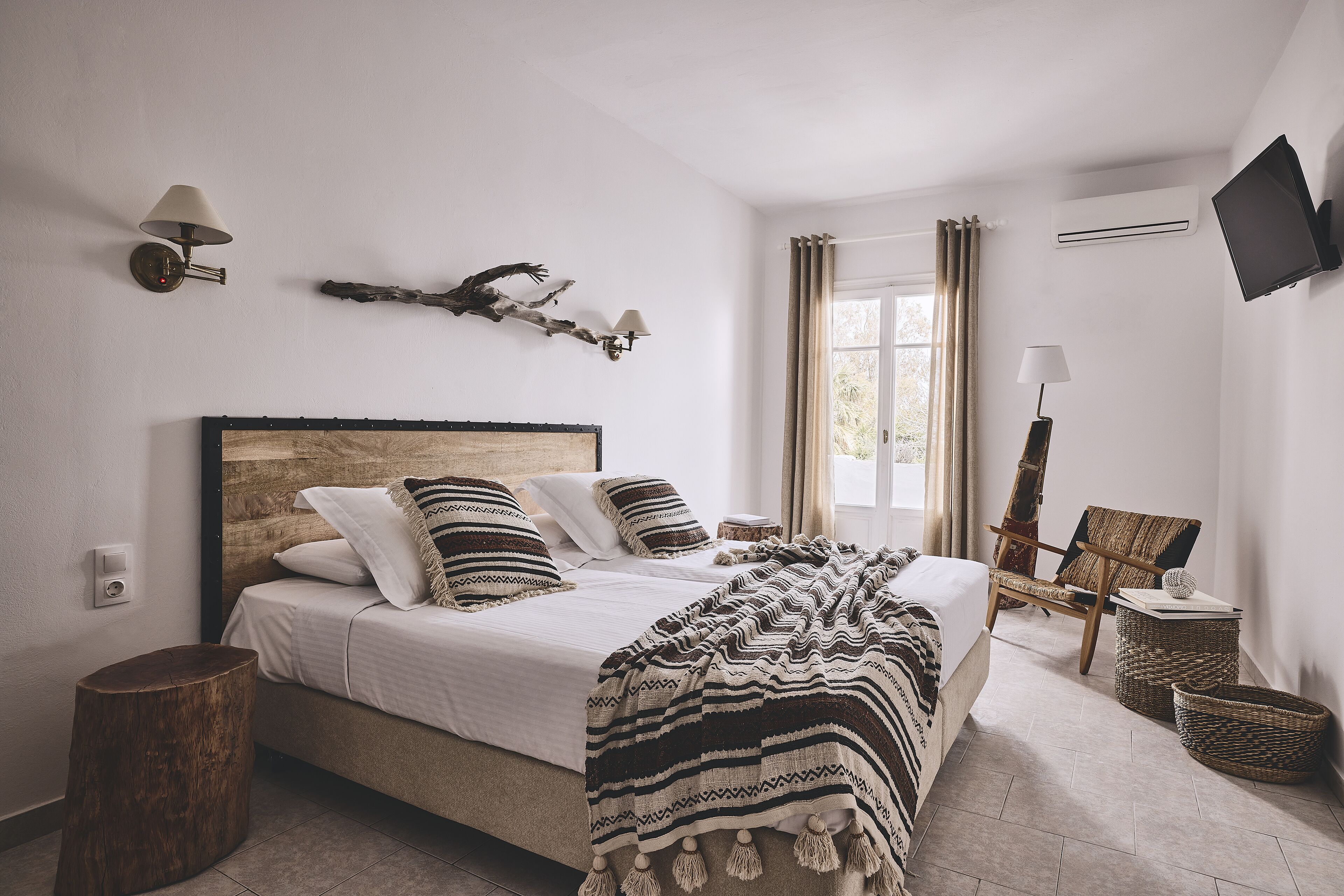 A bedroom with a bed, bedside lamps, a mounted TV, and a window with curtains.