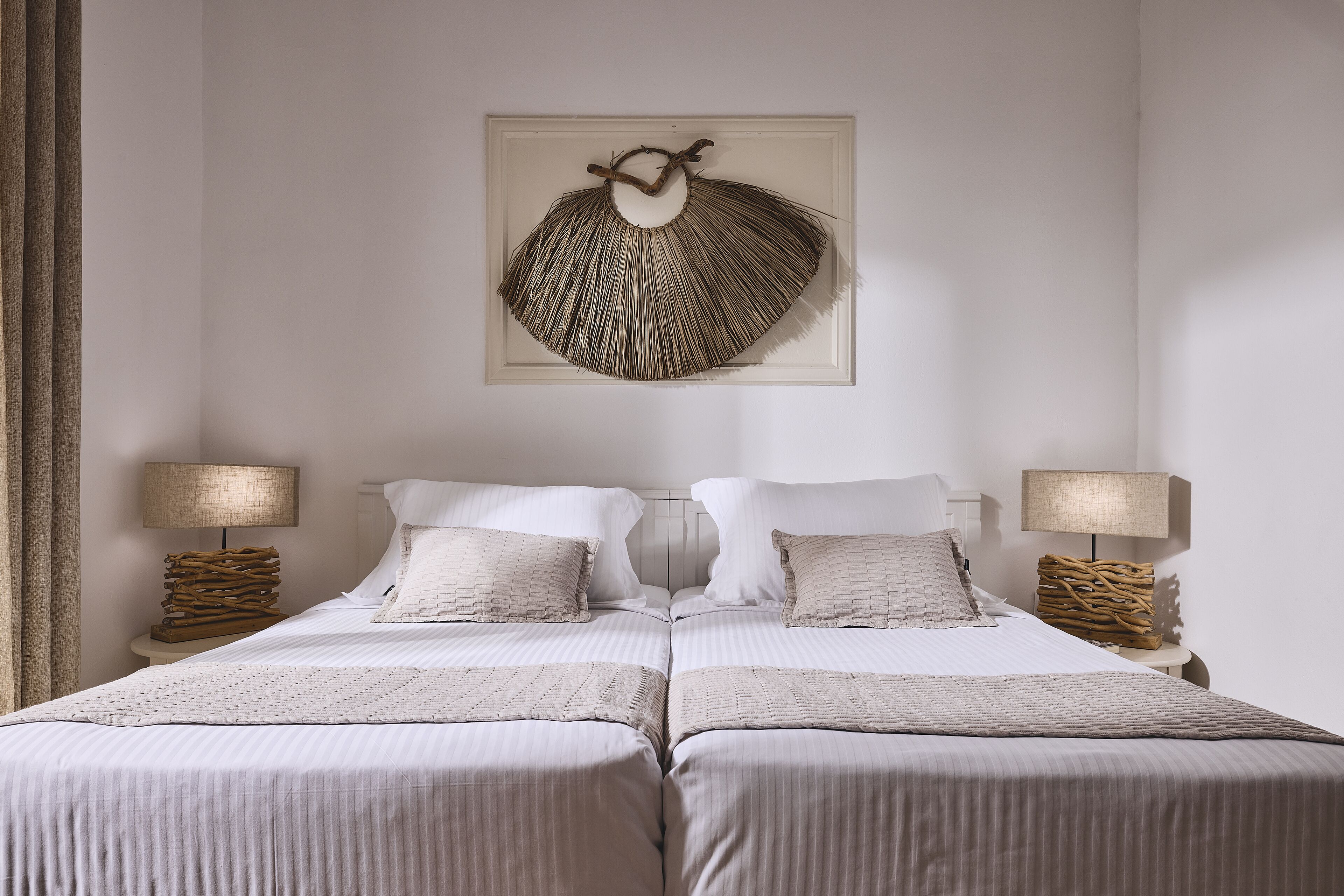 A double bed with a white and beige striped bedspread, two bedside tables with lamps, and a wall-mounted decorative piece.