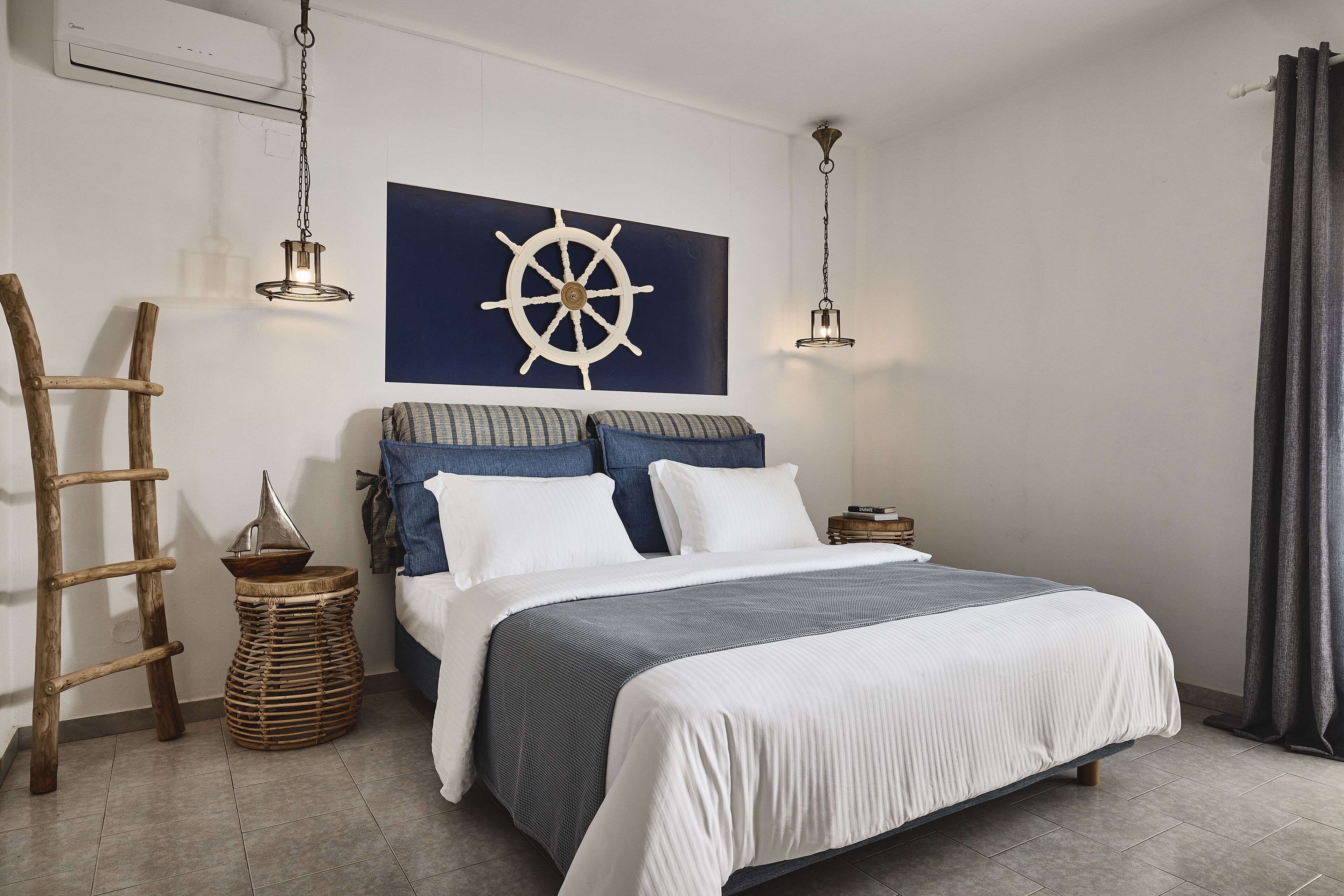 Une chambre à coucher bien rangée, avec un lit, un gouvernail de bateau fixé au mur, deux lampes suspendues, une échelle en bois et un petit tabouret en osier.