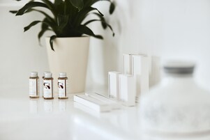 A clean, minimalist setup with a potted plant, three small bottles, and a few white boxes on a reflective surface.