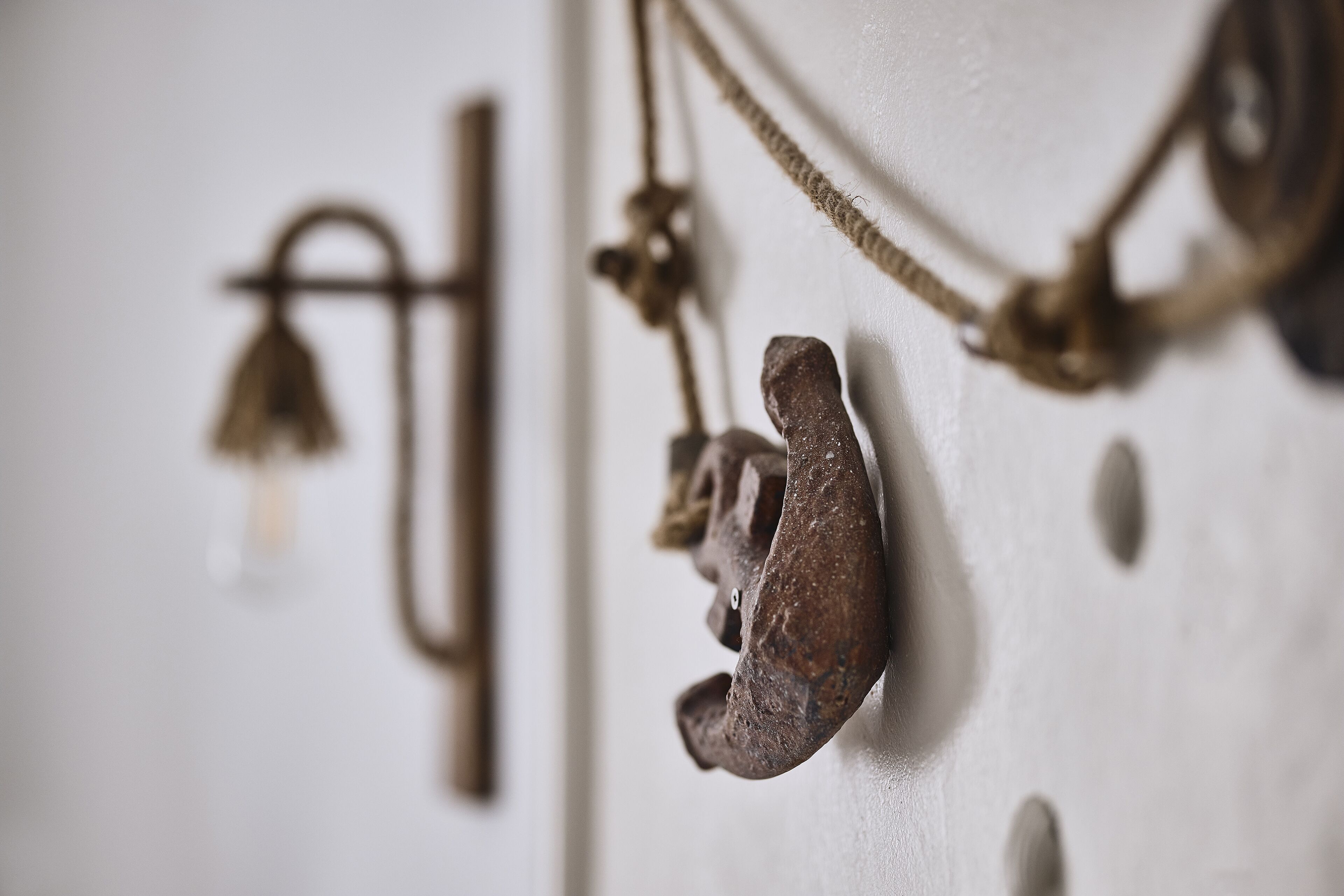 A close-up of a rustic wall with a rustic bell, a metal hook, and a rope.