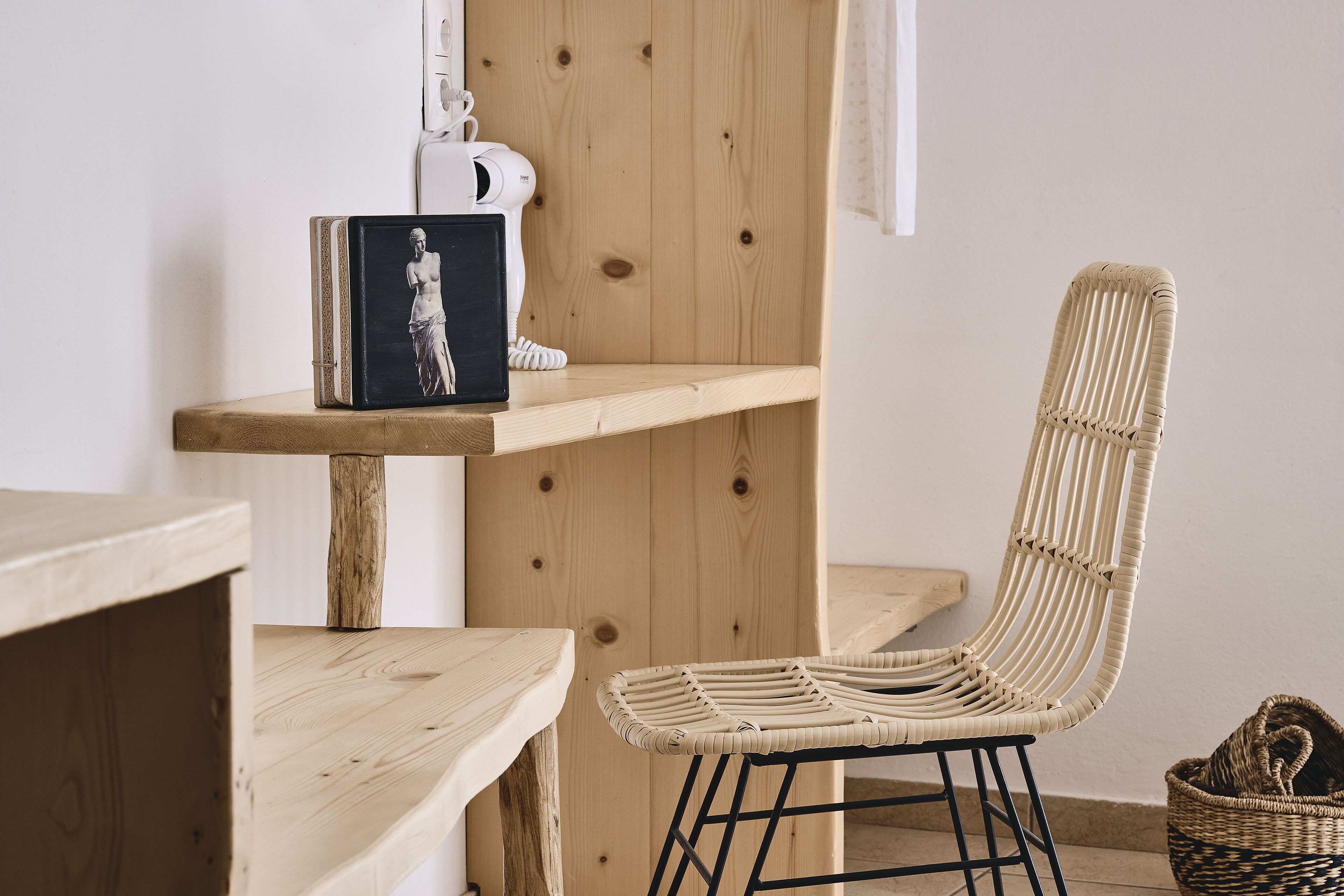 Una habitación con estantería de madera, una silla de mimbre y una cesta de mimbre.