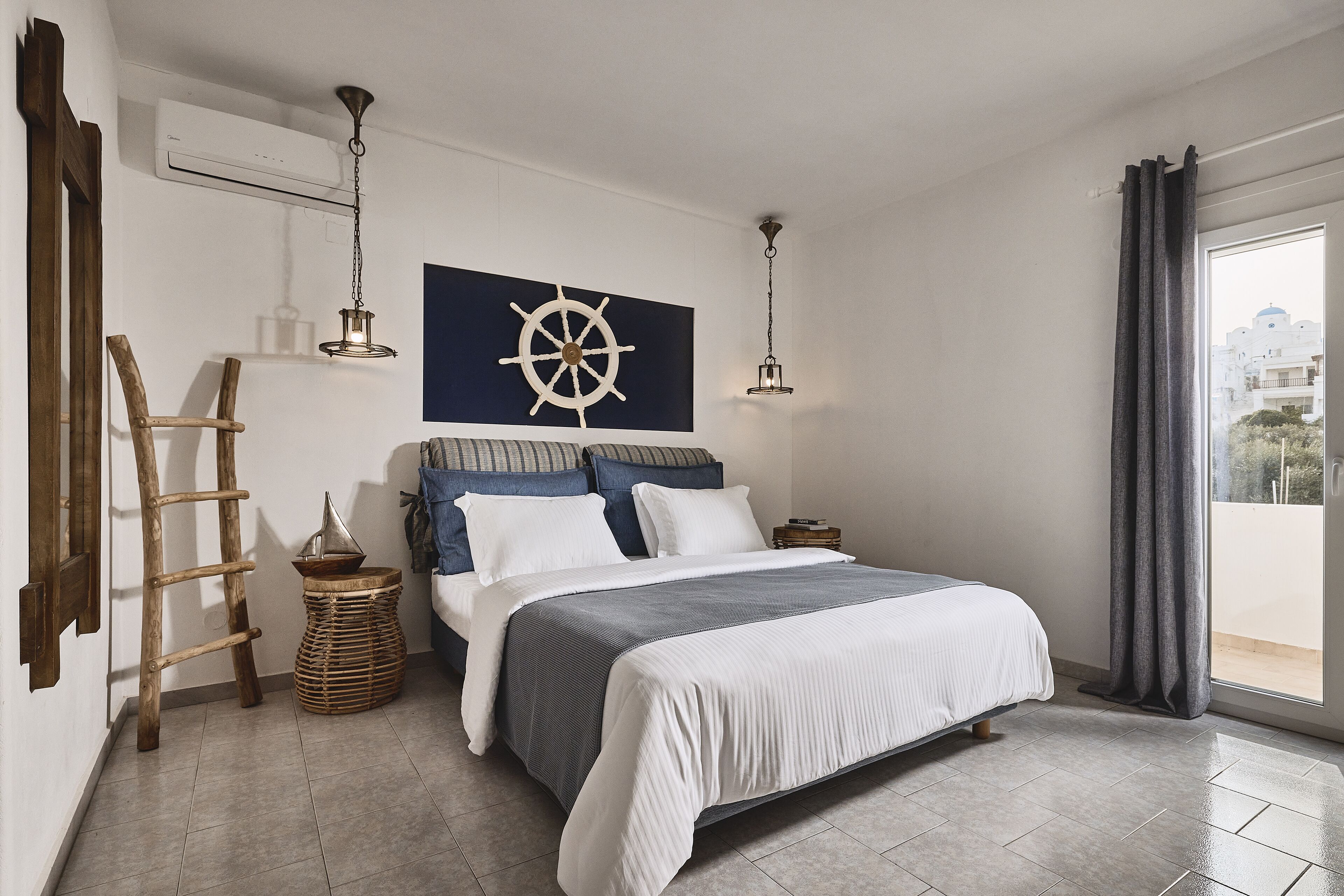 Een slaapkamer met een groot bed, een houten trap, een decoratie van een scheepswiel en uitzicht op een gebouw door het raam.