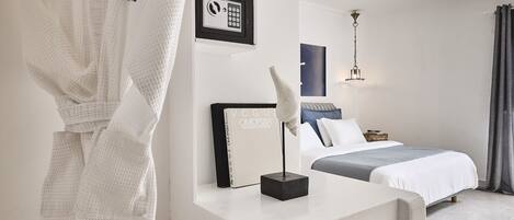 A hotel room with a bed, a desk with a lamp, a robe hanging on the wall, and a framed picture of a security keypad.