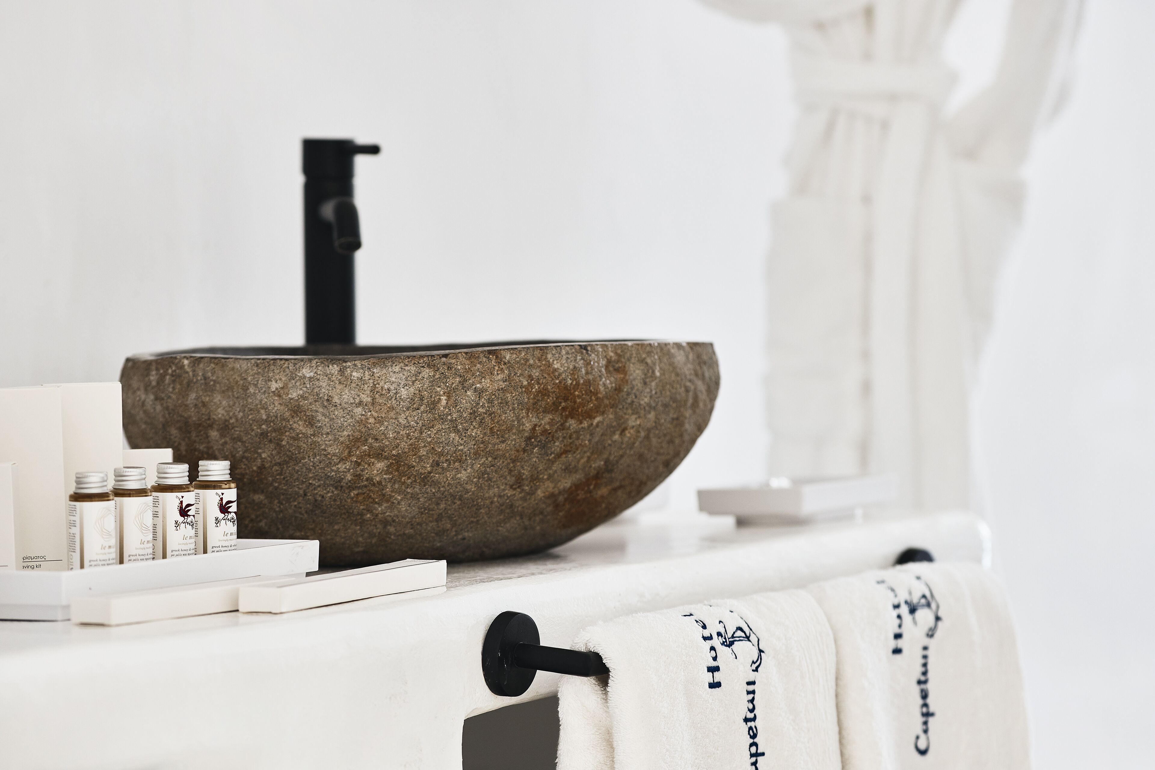 A bathroom with a stone basin, a black faucet, and neatly arranged toiletries.