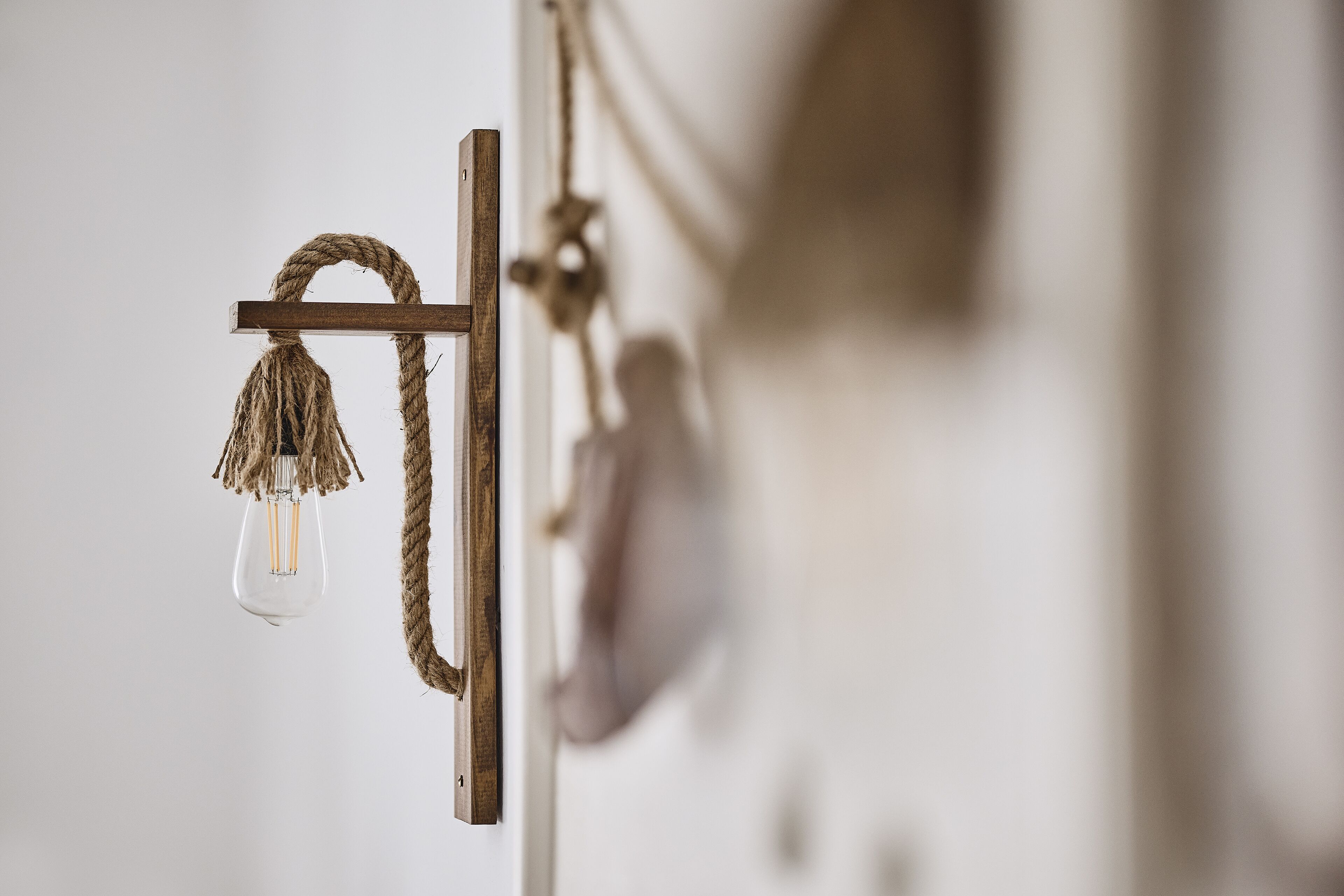 A rustic wall-mounted light fixture with a clear glass bulb and a rope.