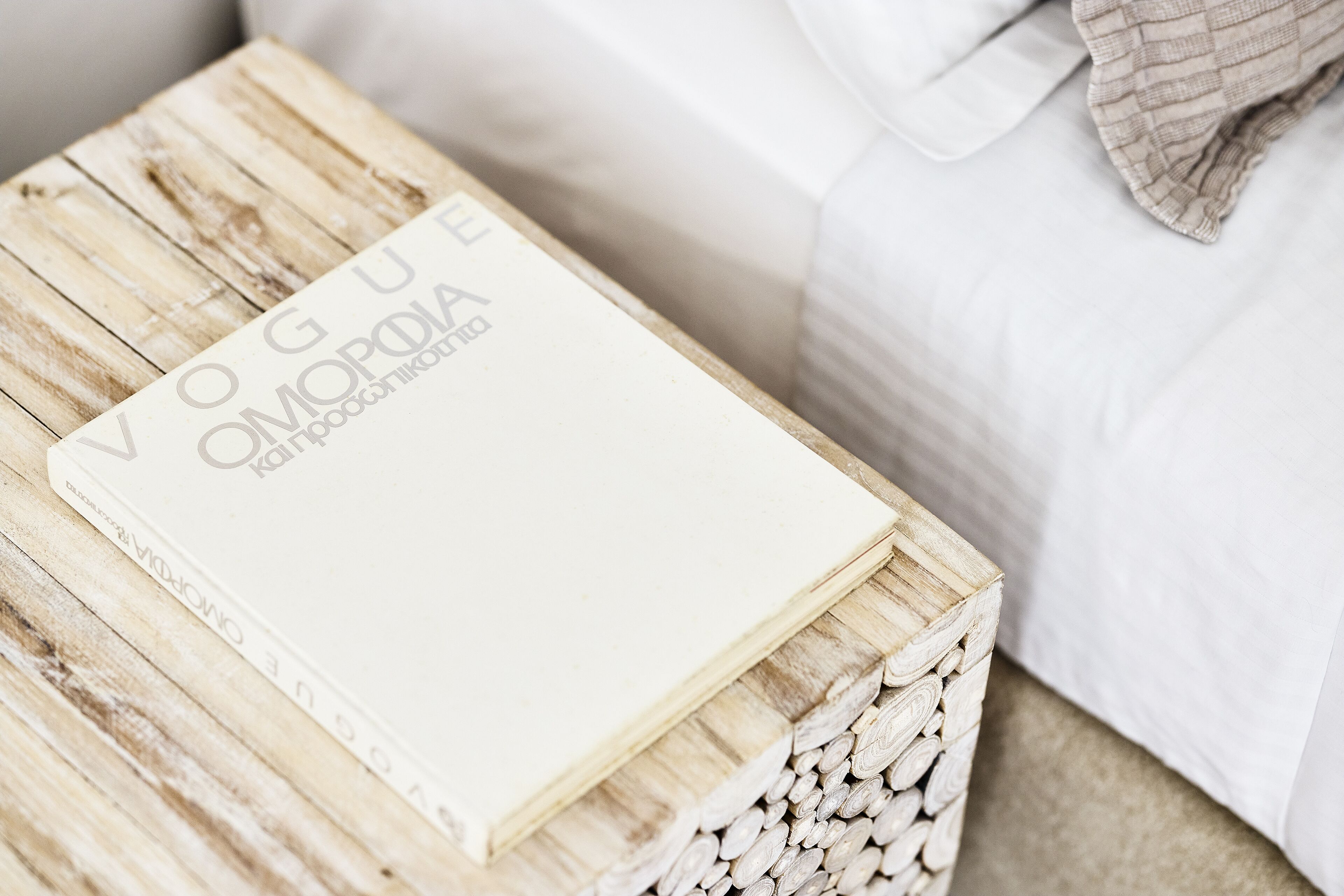 A magazine titled 'Vogue Omopodia' on a wooden table next to a bed.
