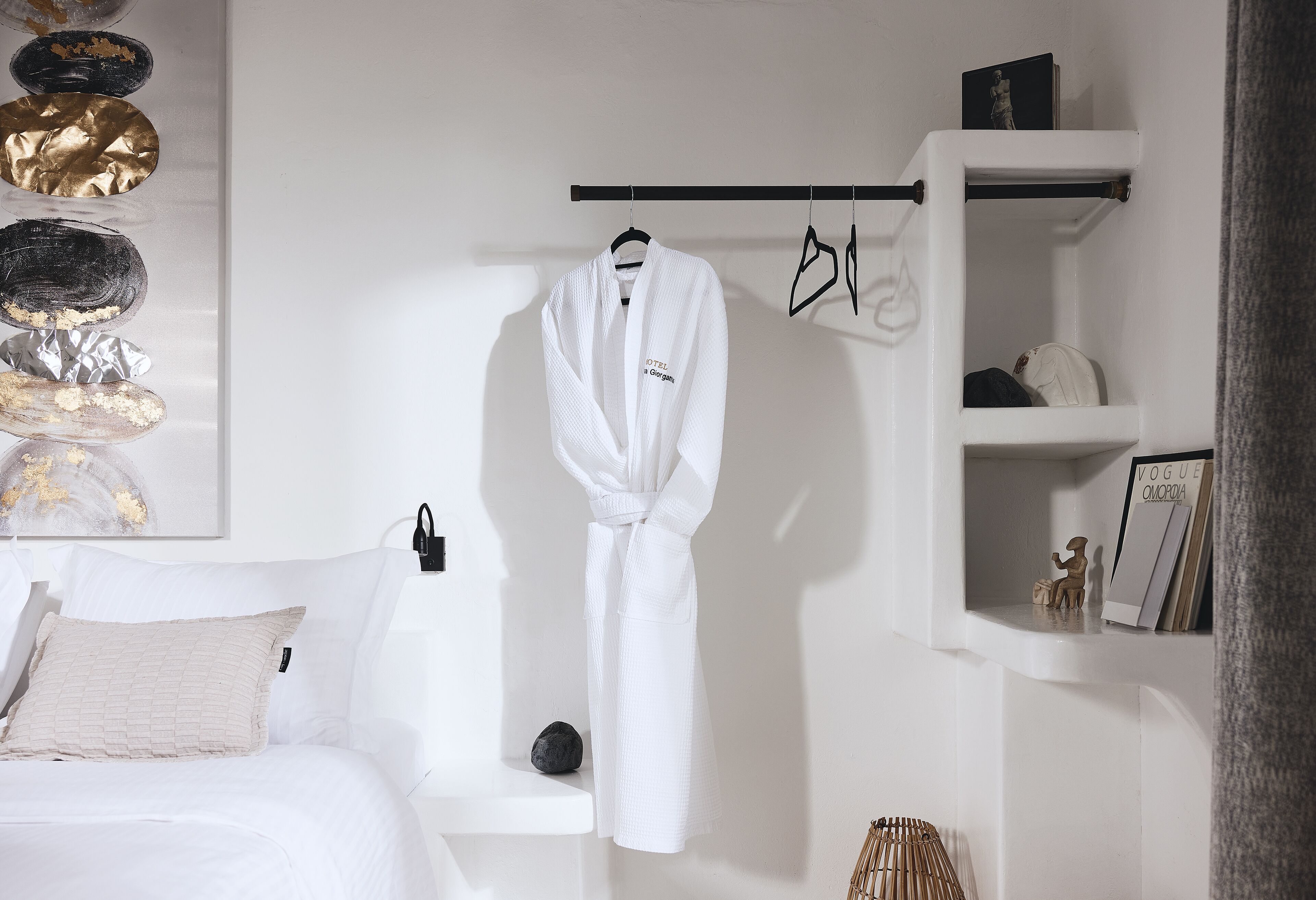 Een witte badkamer met een badkuip, een badjas hangend aan een rek, en een plankje met een boek en een beeldje.