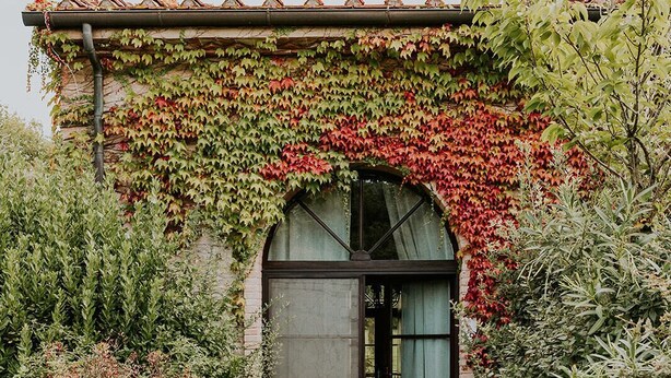 A building with a brick facade, a tiled roof, and a large arched doorway. - Ginestriccio (Bibbona)