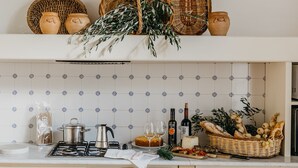 A kitchen with a tiled backsplash, a gas stove, a coffee pot, a wine bottle, and various food items. - Ginestriccio (Bibbona)