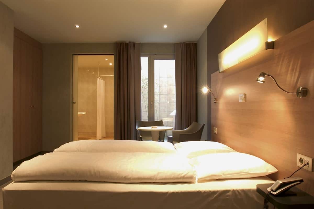 A hotel room with a large bed, a small table, and a shower area.