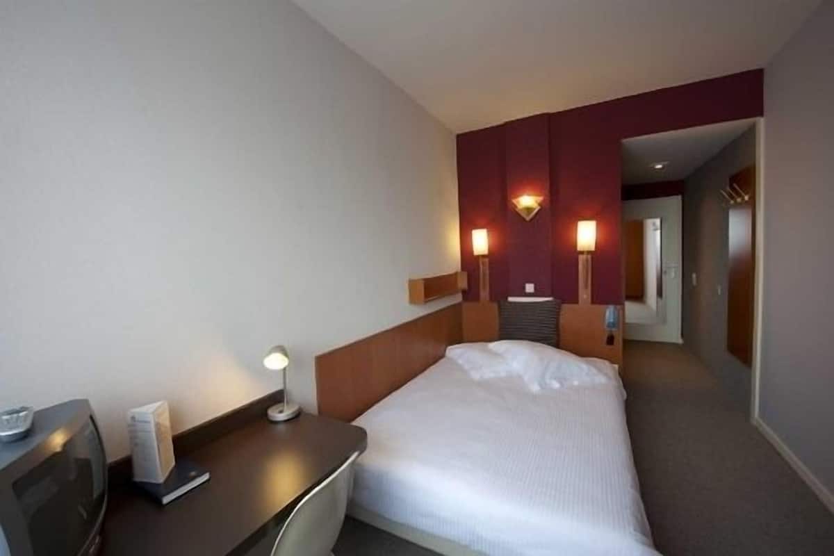 A hotel room with a bed, bedside table, lamp, and a wall-mounted light fixture.