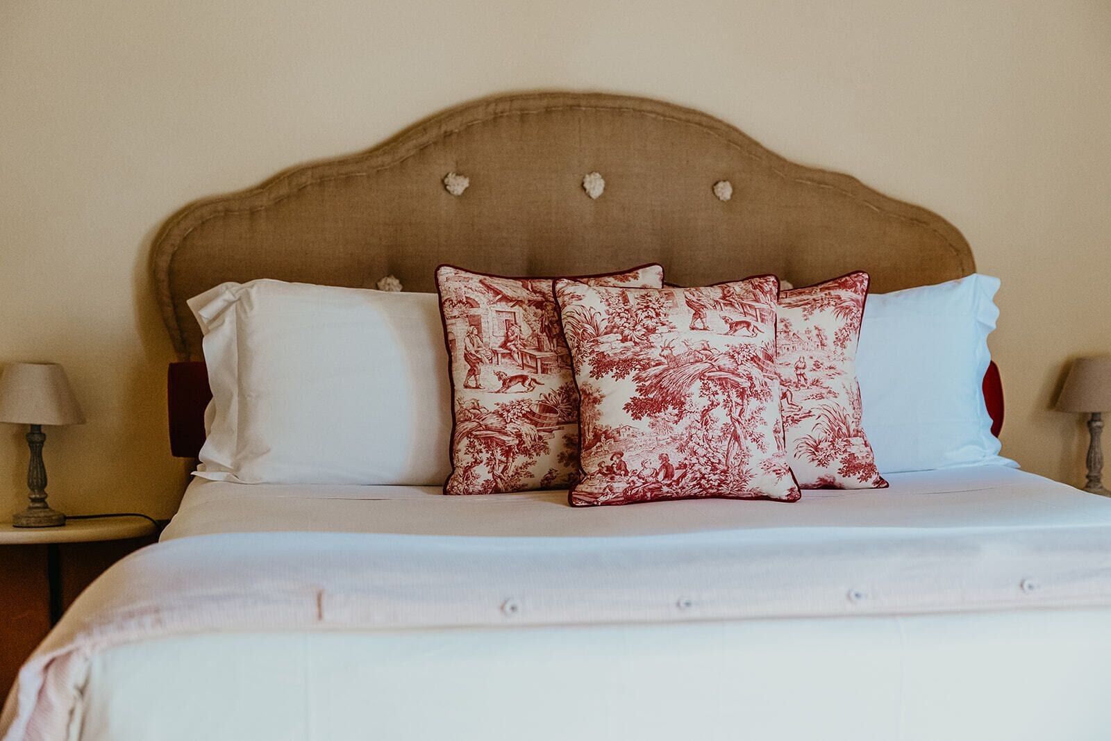 A bed with a headboard, two white pillows, and two red and white patterned pillows.