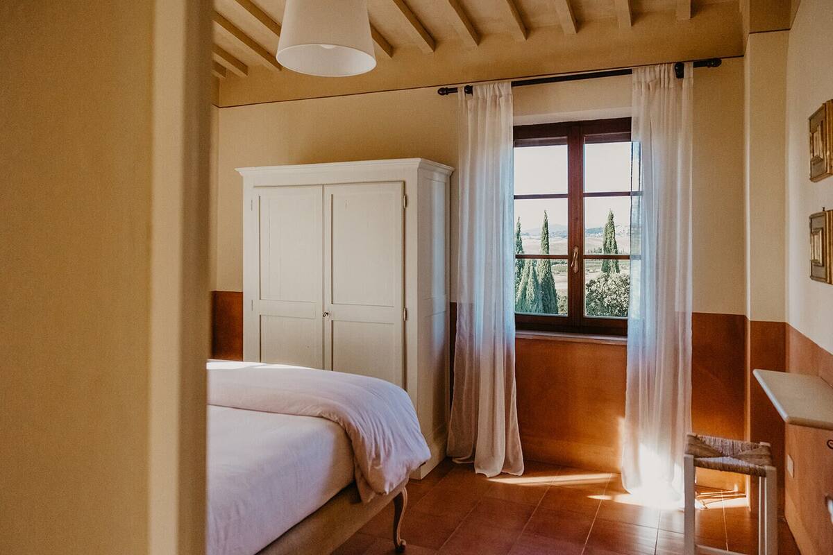 Une chambre à coucher avec un lit, une armoire, un bureau et une fenêtre avec des rideaux.