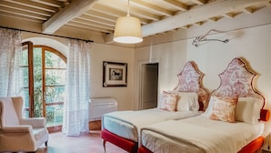 A bedroom with two beds, a chair, a window with curtains, a picture on the wall, and a ceiling fan. - Poggio Cornetto (Bibbona)