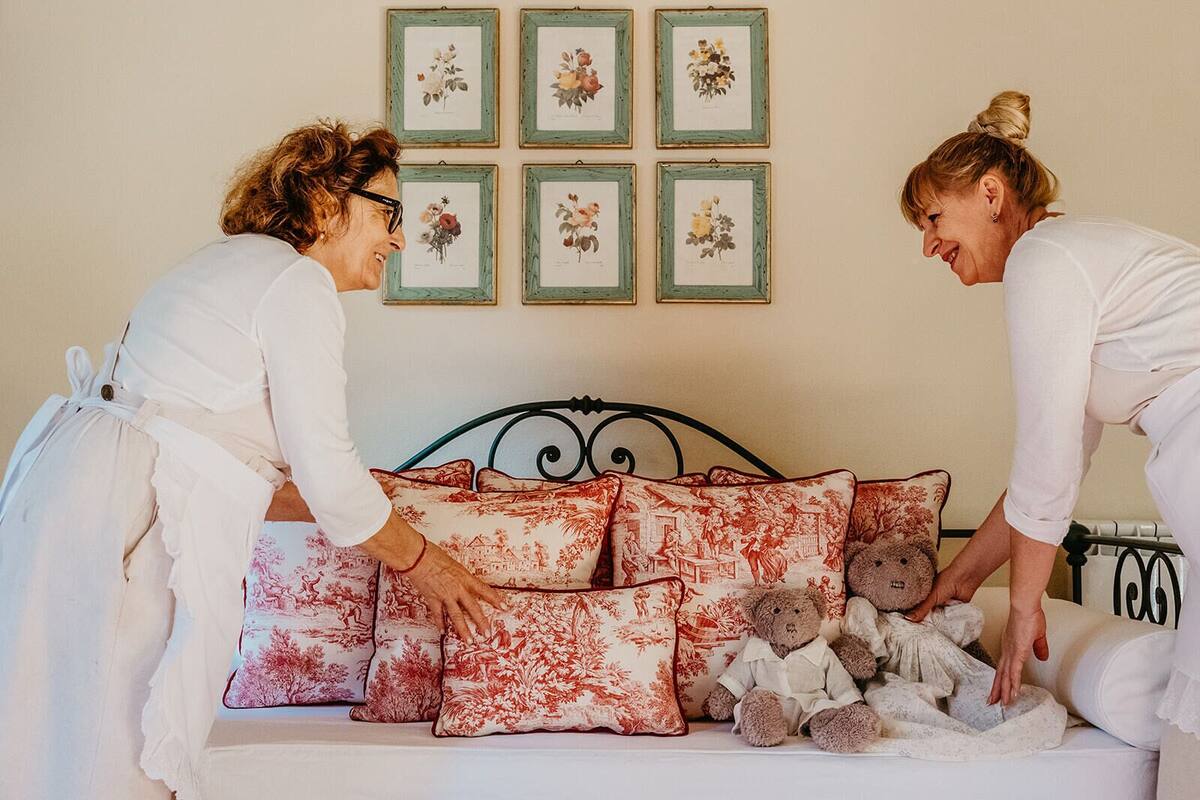 Une chambre à coucher avec un lit, des coussins à motifs floraux et des reproductions botaniques encadrées accrochées au mur.
